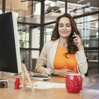 woman sitting at desk smiling, while on a phone call.