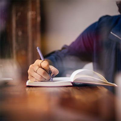 Close up of woman sitting at desk, writing in journal.