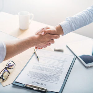 People shaking hands over a desktop with a signed contract on it.