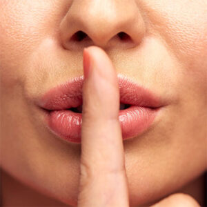 woman holding her index finger in front of her lips in a "Shhh" gesture.