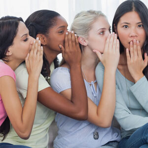 Four women whispering to each other as if in a line in the game "telephone."