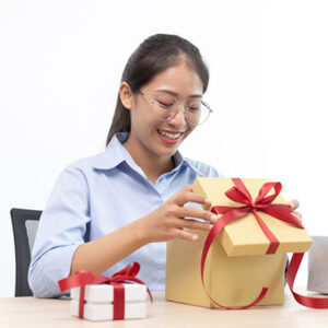 Woman opening box with ribbon on it, smiling at what she sees inside.