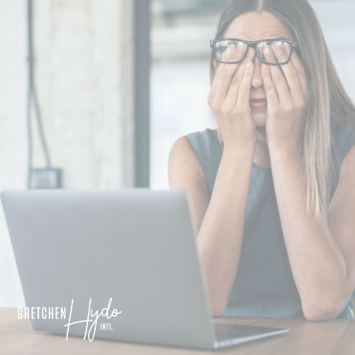 woman rubbing her tired eyes while sitting at desk with open laptop