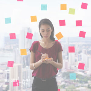 Woman standing and writing on post-it notes while standing in front of a glass wall that's covered in post-it notes.
