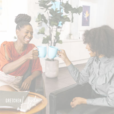 Two women sitting together, drinking coffee and laughing.